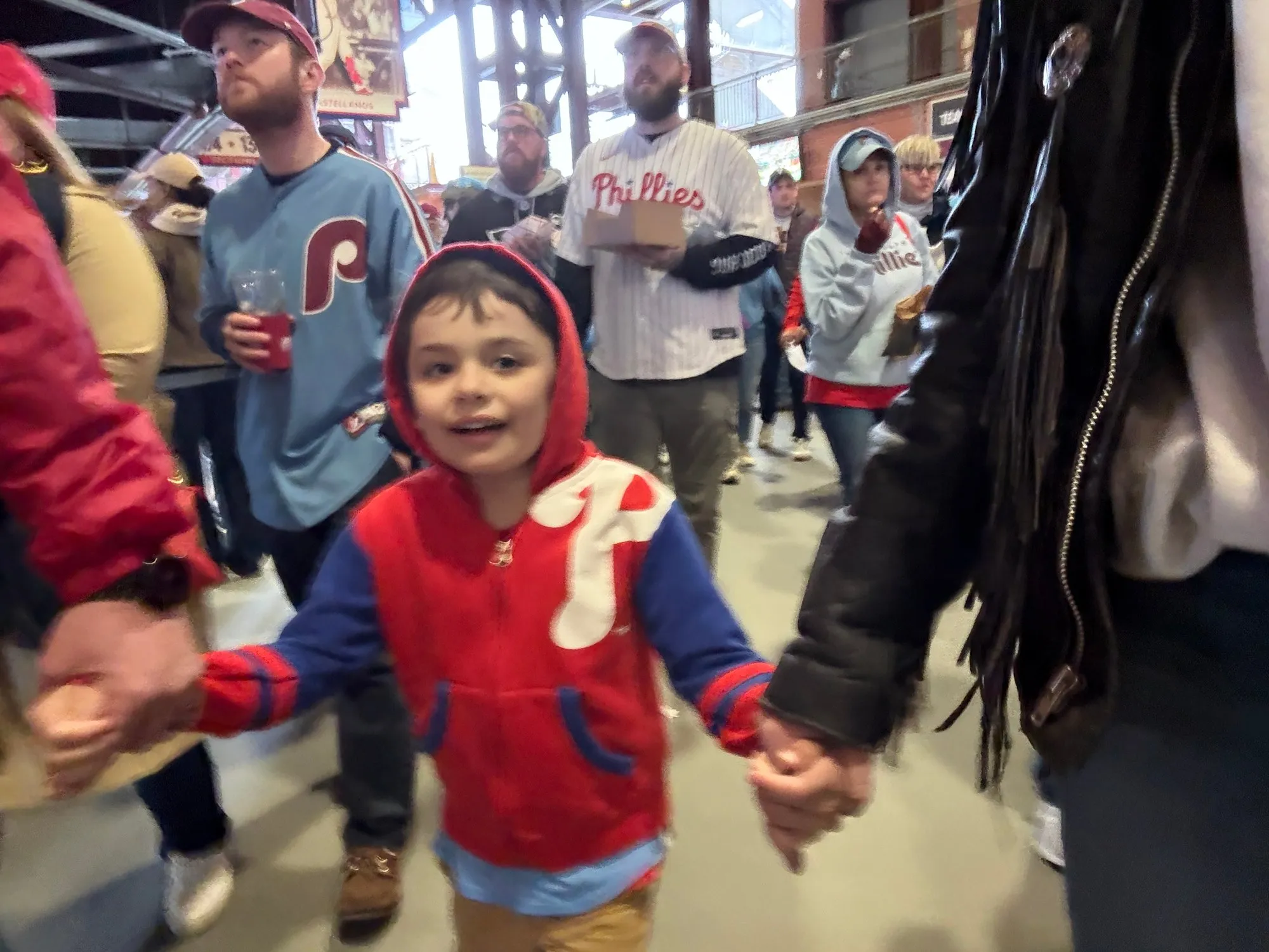 Remy in a red Phillies hoodie, holding hands as he walks through the crowd at Citizens Bank Park